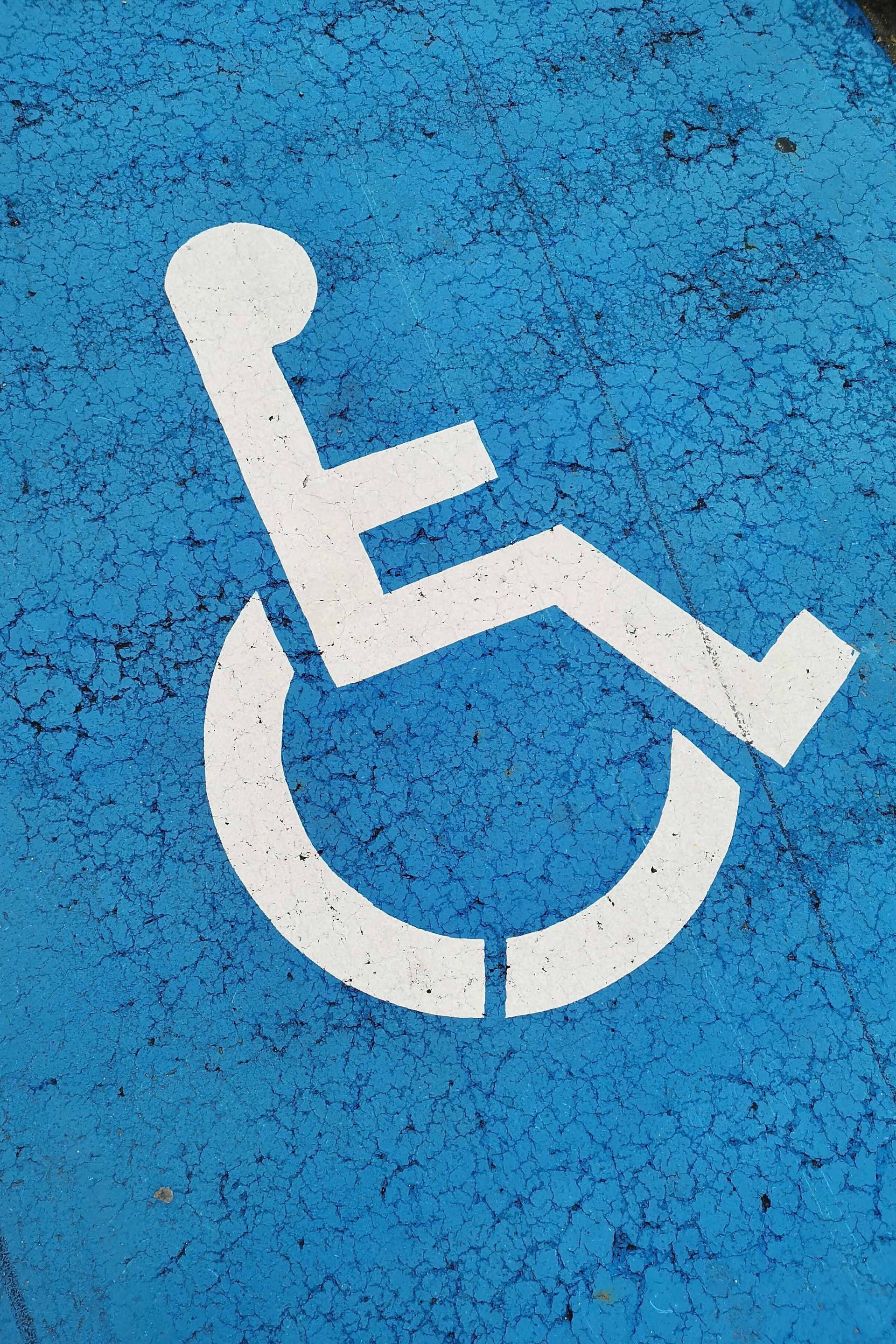 White wheelchair accessibility symbol painted on blue pavement.