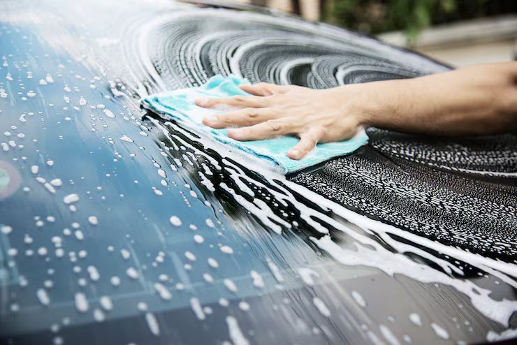 Hand washing a black car windshield with soapy foam and a blue sponge