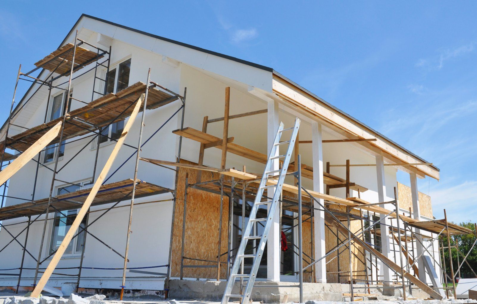 House under construction with scaffolding against white stucco exterior, blue sky.