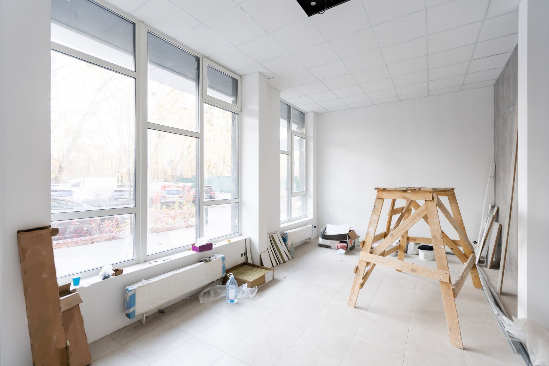 Empty room under renovation with large windows and a wooden ladder.