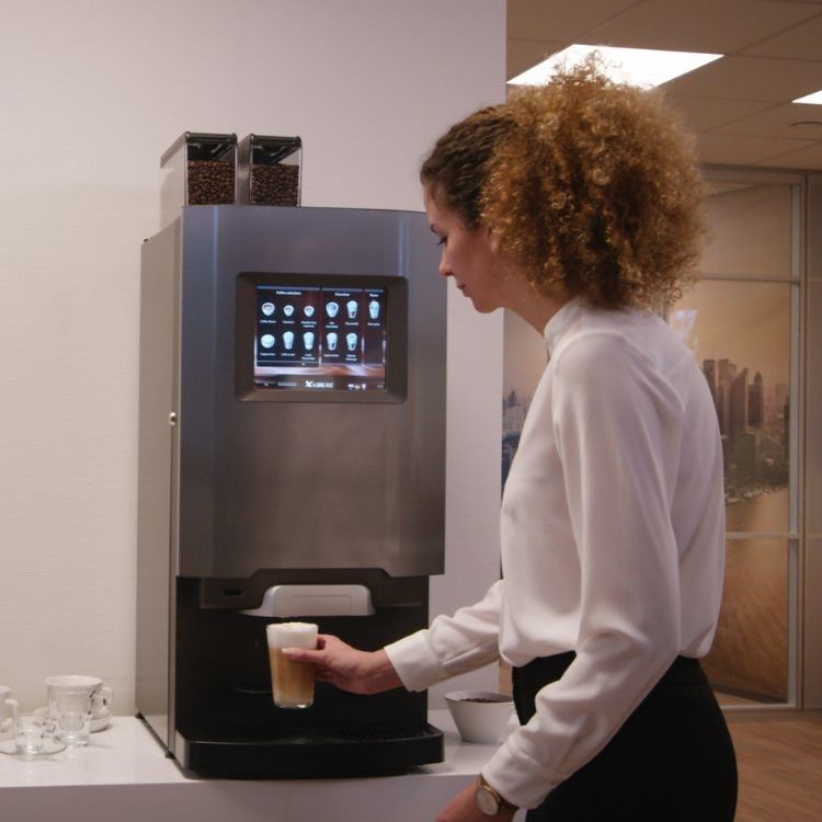 Woman selecting a drink from a coffee machine in an office setting.