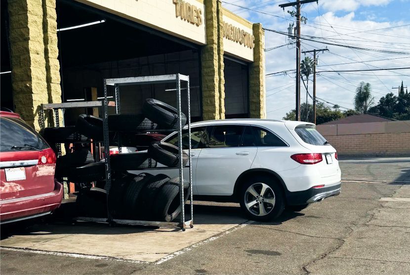 White SUV parked at an auto repair shop bay beside a red car, with equipment in the open garage. | One Stop Auto Service