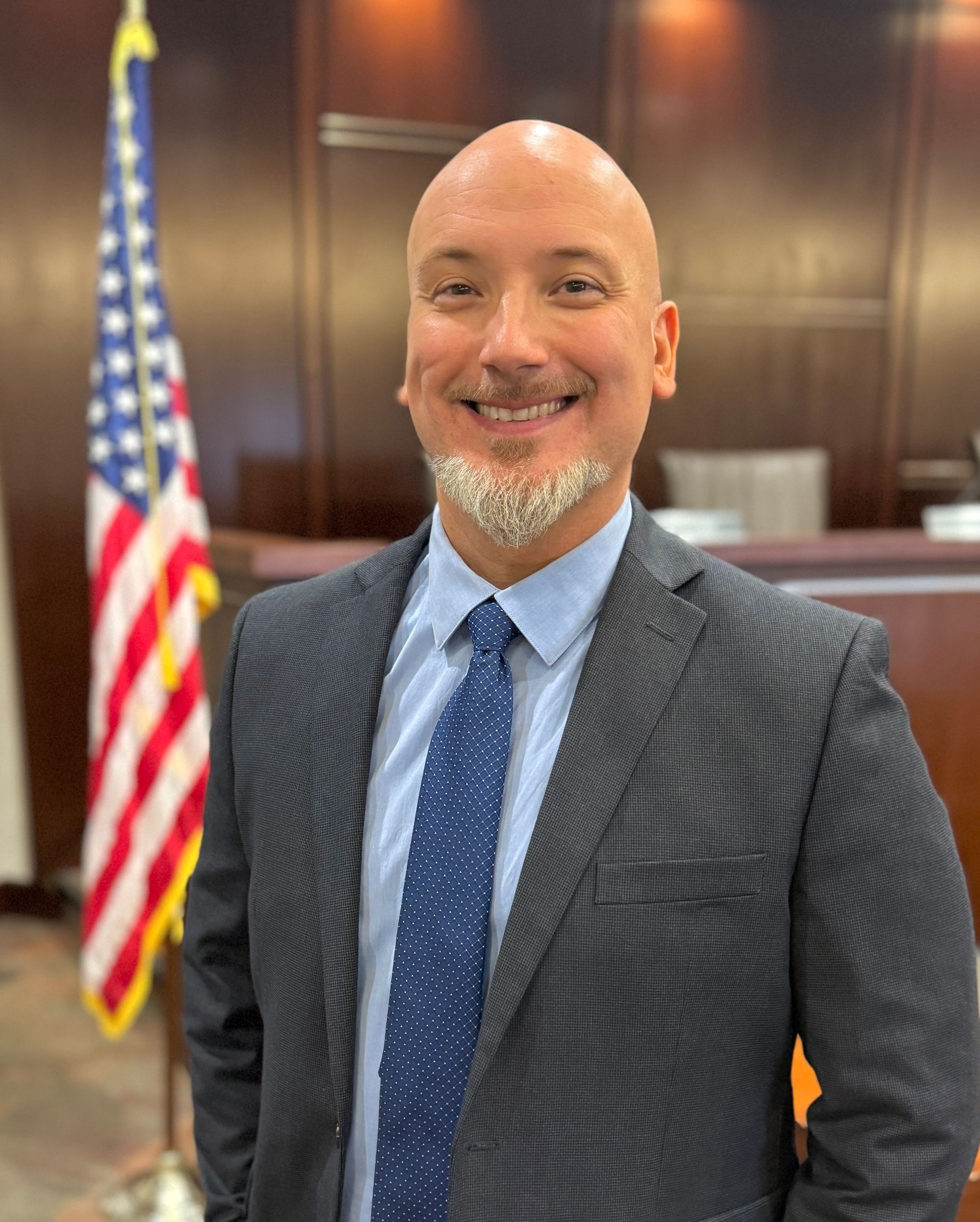 A man in a suit and tie is standing in front of an american flag.