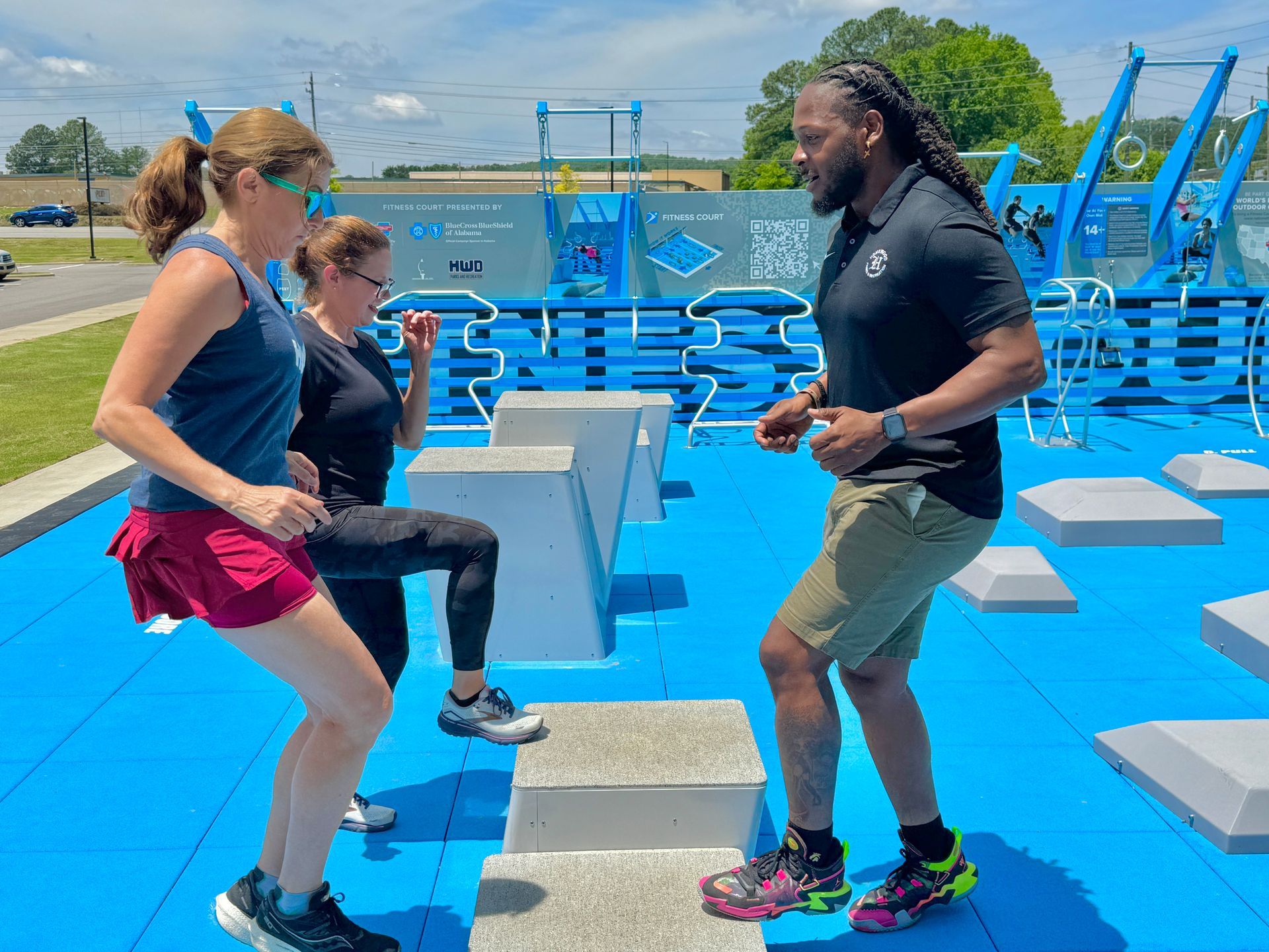A man and two women are doing squats on steps in a park.