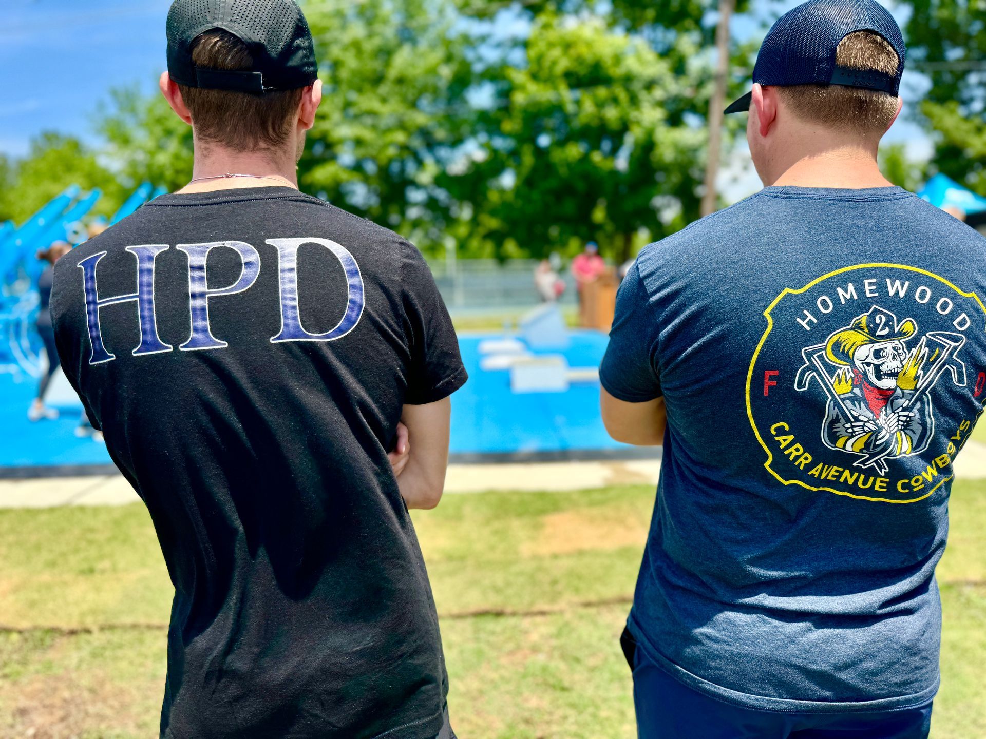 Two men wearing hpd shirts are standing next to each other in a park.