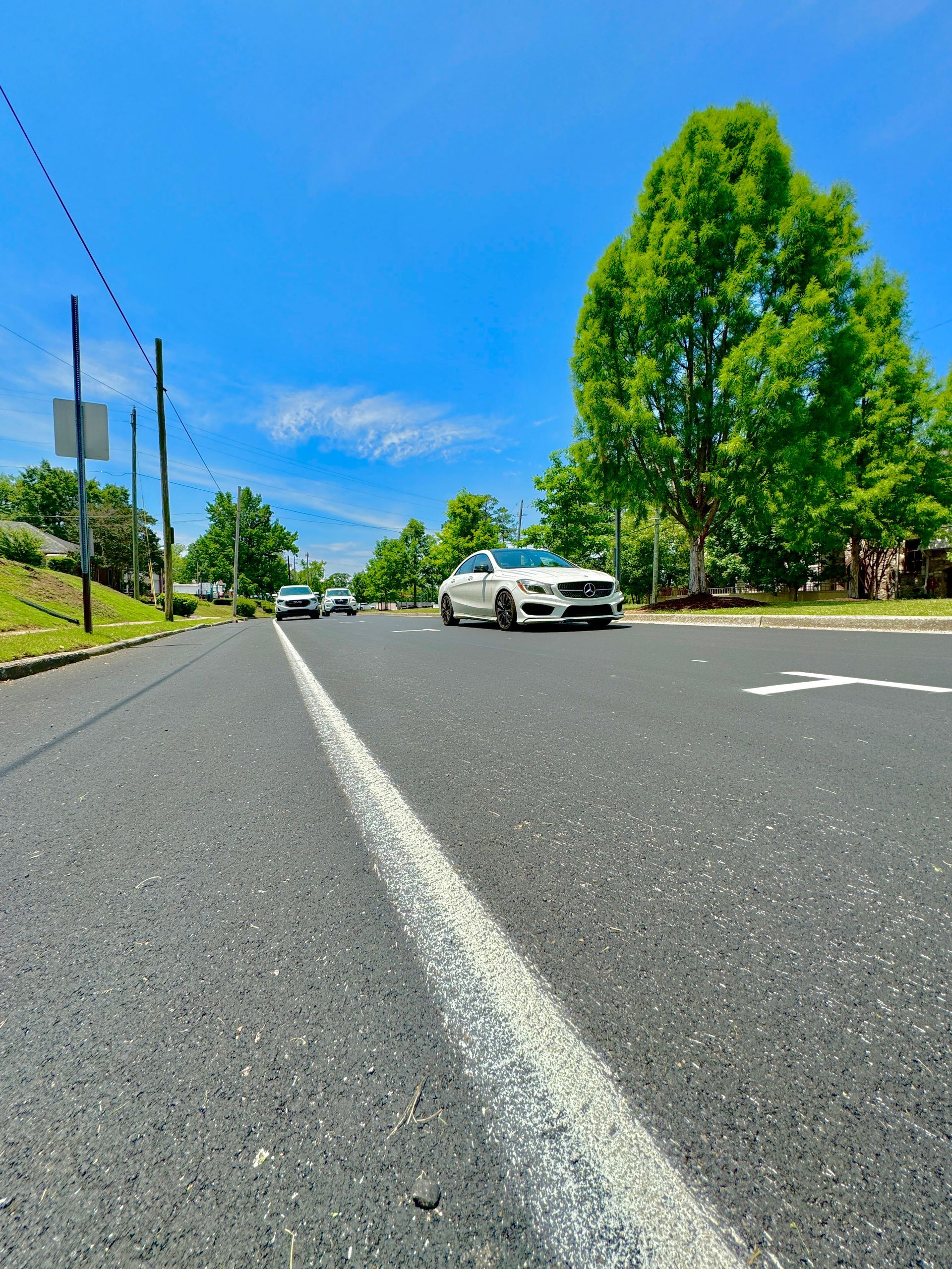 A white car is driving down a street with trees in the background