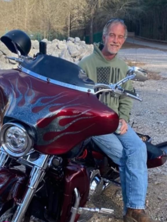 A man is sitting on a red motorcycle wearing a green shirt with an american flag on it