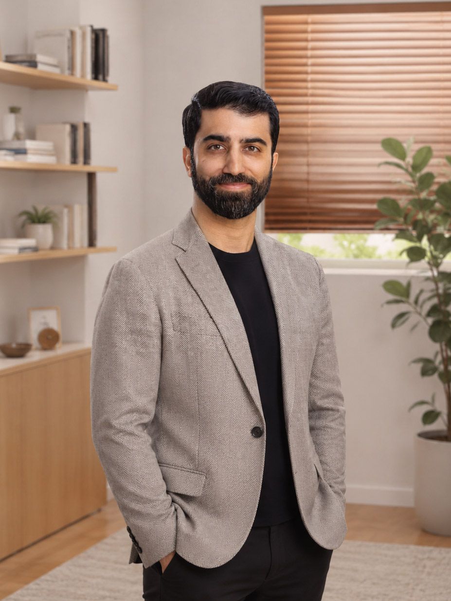 Dr. Khashayar Nattagh, MD in a gray blazer standing in a bright room with shelves, a plant, and window blinds