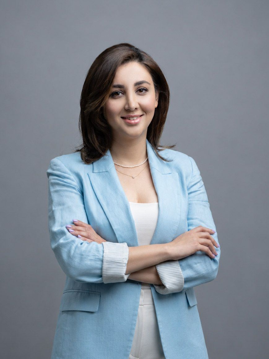 Dr. Pari Mokhtari in a light blue blazer smiling with arms crossed against a gray background