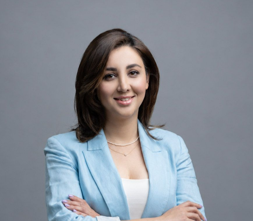 Smiling professional in a light blue blazer with arms crossed against a gray background