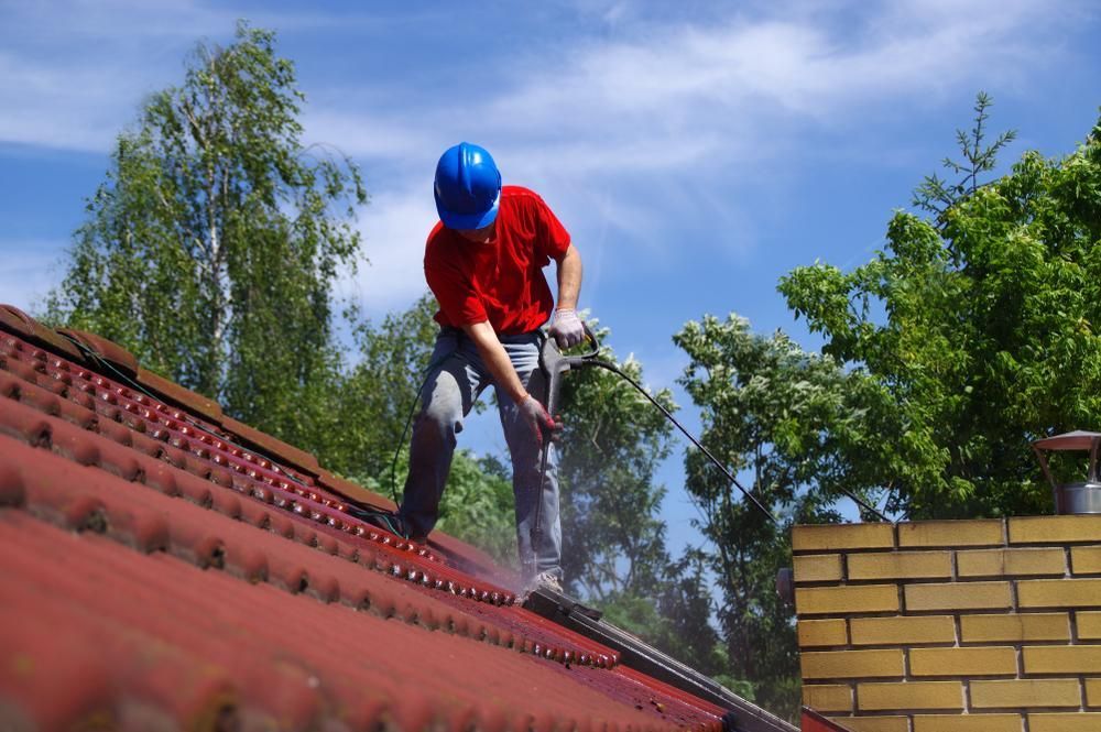 A Man Is Cleaning The Roof Of A House With A High Pressure Washer — Roofworx Group In Bathurst, NSW