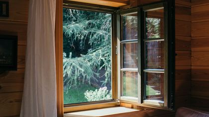 A wooden house with an open window looking out to a forest.