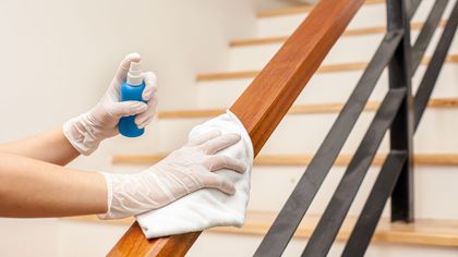 A person wearing gloves is cleaning a wooden railing with a cloth.