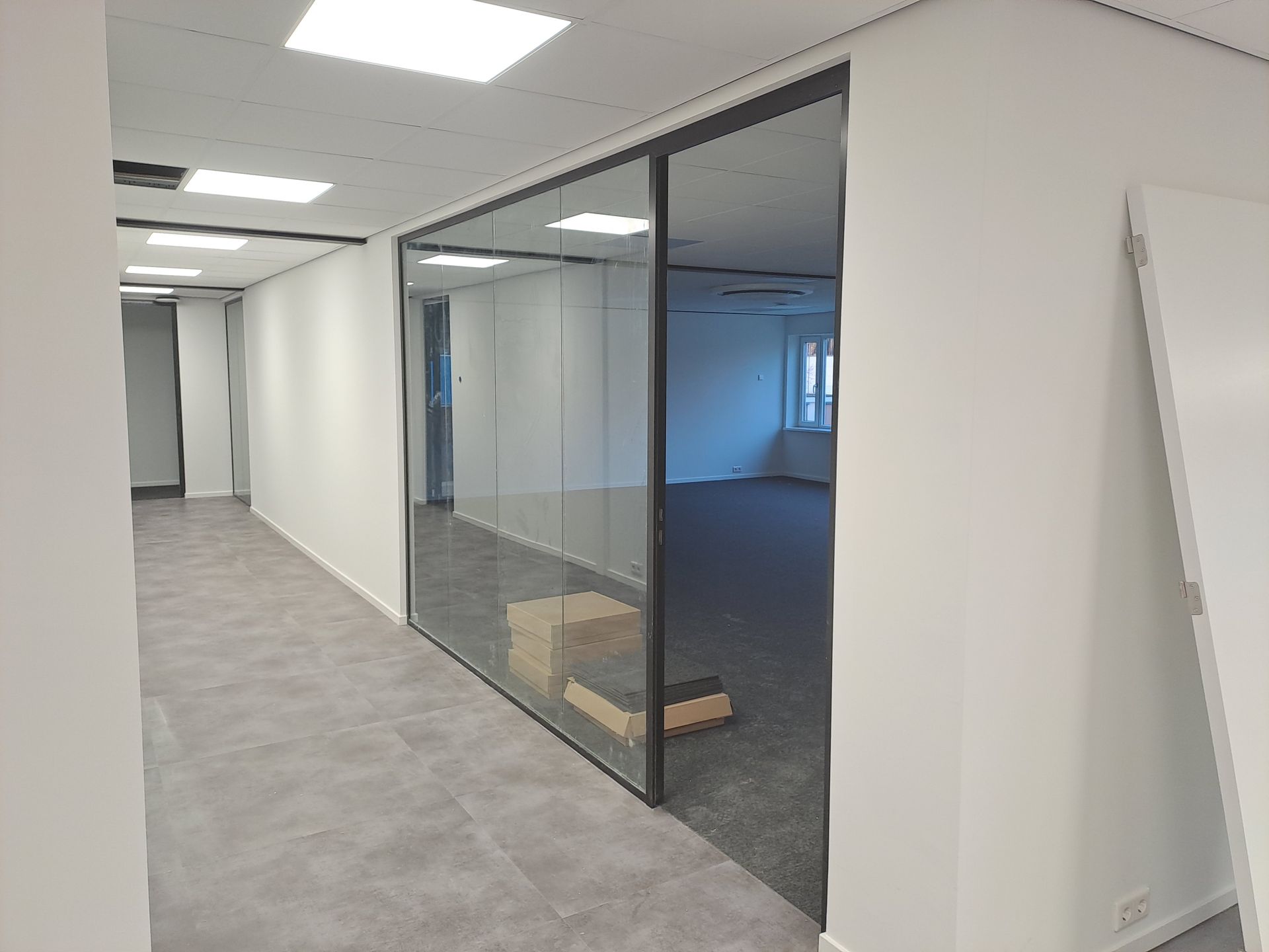 Een leeg kantoor met een glazen wand en vloerbedekking.