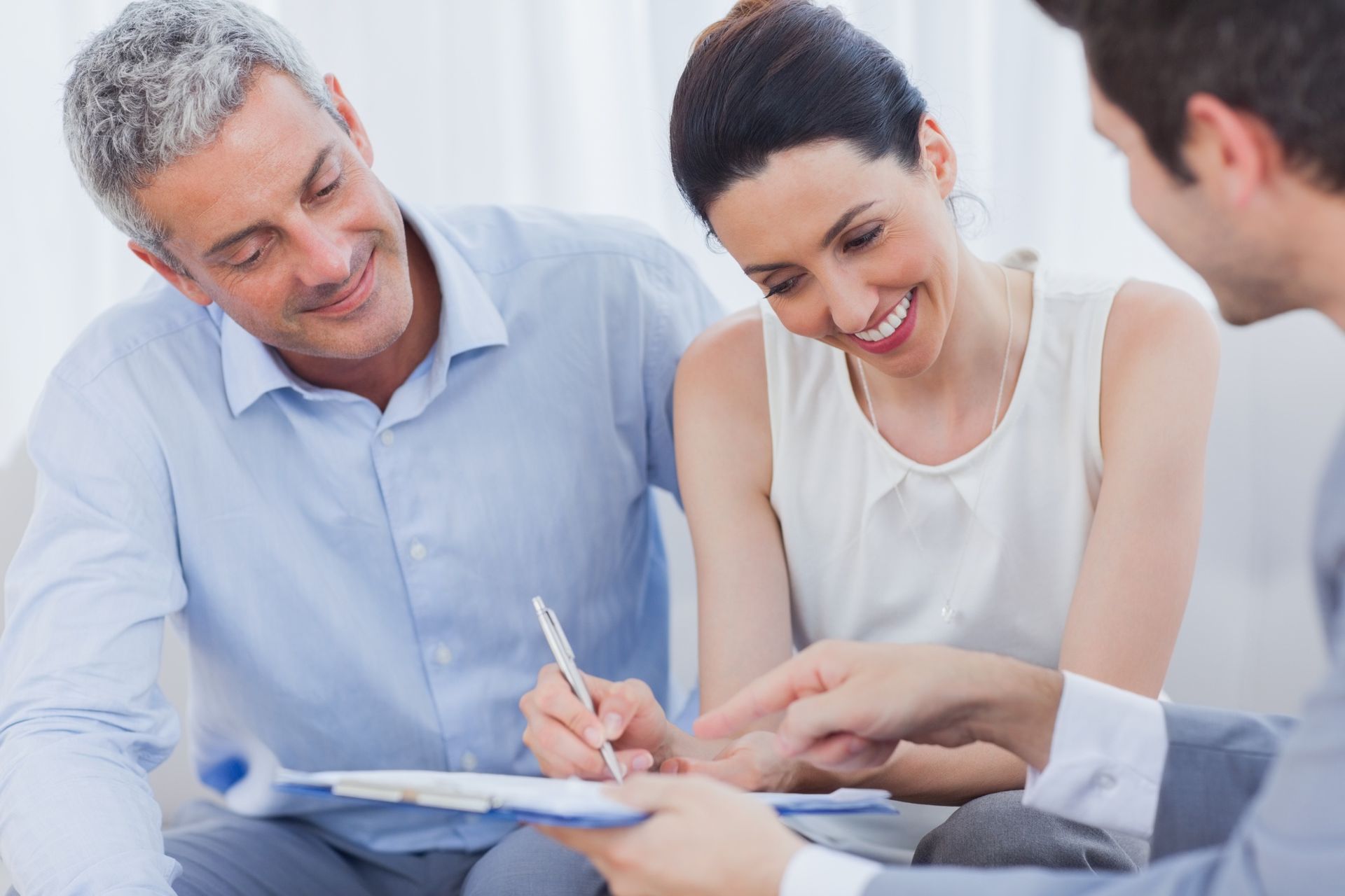 Couple signs document, smiling, assisted by advisor in office.