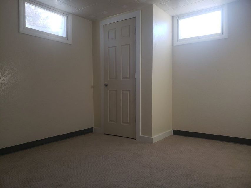 Empty beige room with carpet, a closed door, and two small high windows