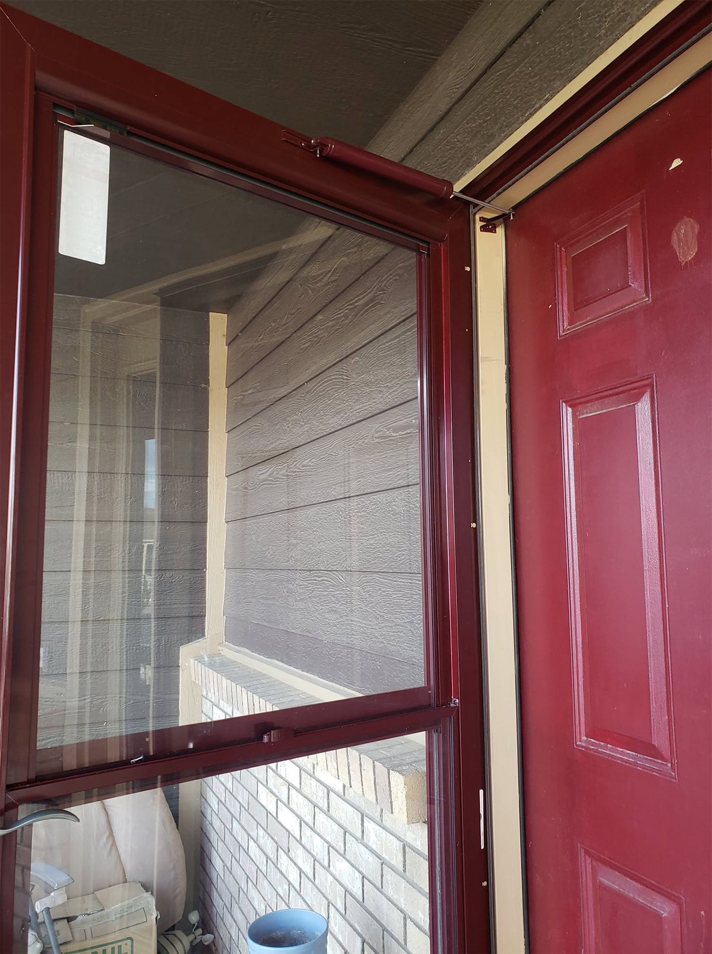 Open red front door and screen door leading to a small porch with white brick siding.