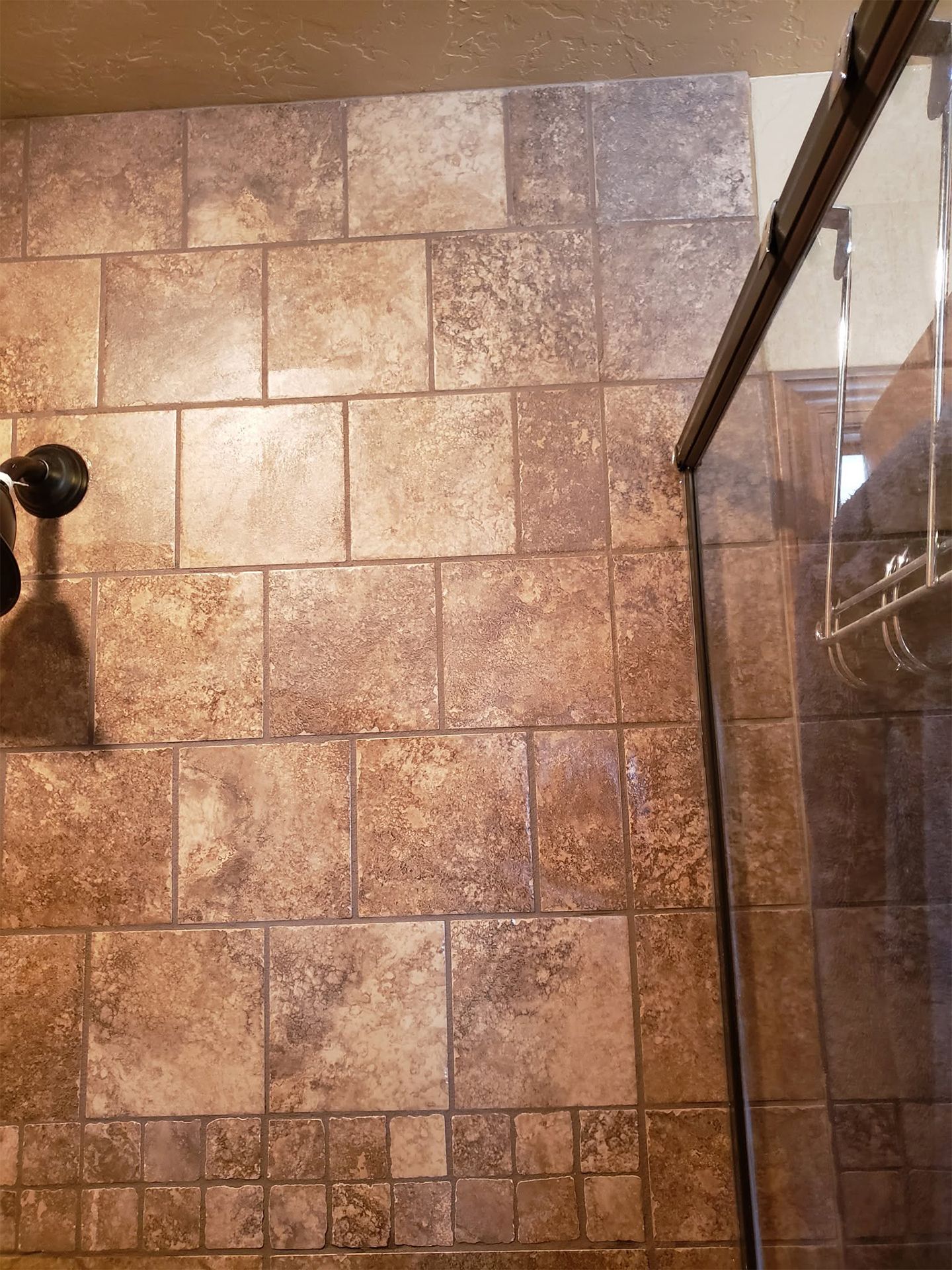 Tiled shower wall and glass door with chrome frame and black showerhead handle
