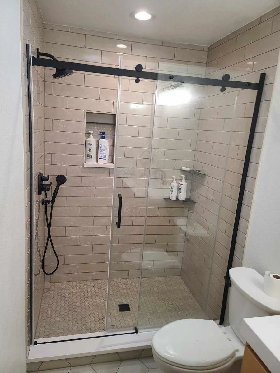 Modern walk-in shower with glass doors, beige tile, black hardware, and a toilet beside it