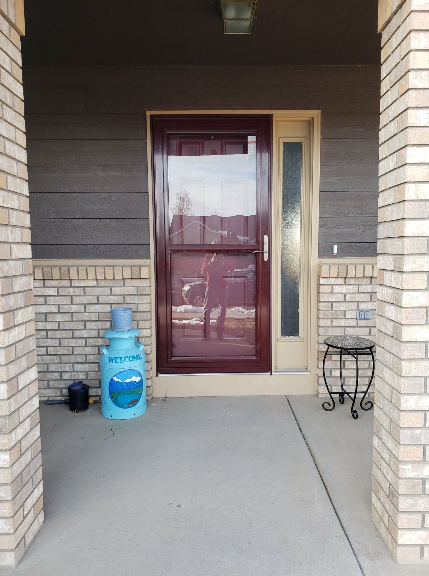 Front porch with a maroon door, brick pillars, blue water jug, and small table under a covered entryway
