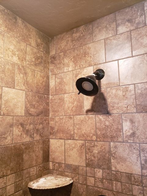 Tiled shower corner with a mounted black showerhead and a small stone shelf below.