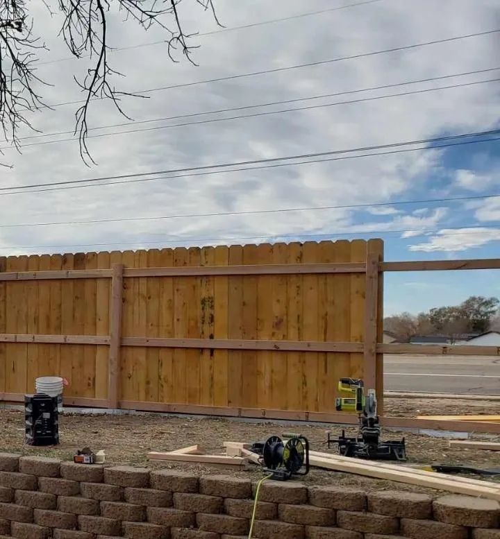 Wooden fence under construction with tools and lumber in a backyard, under a cloudy sky.