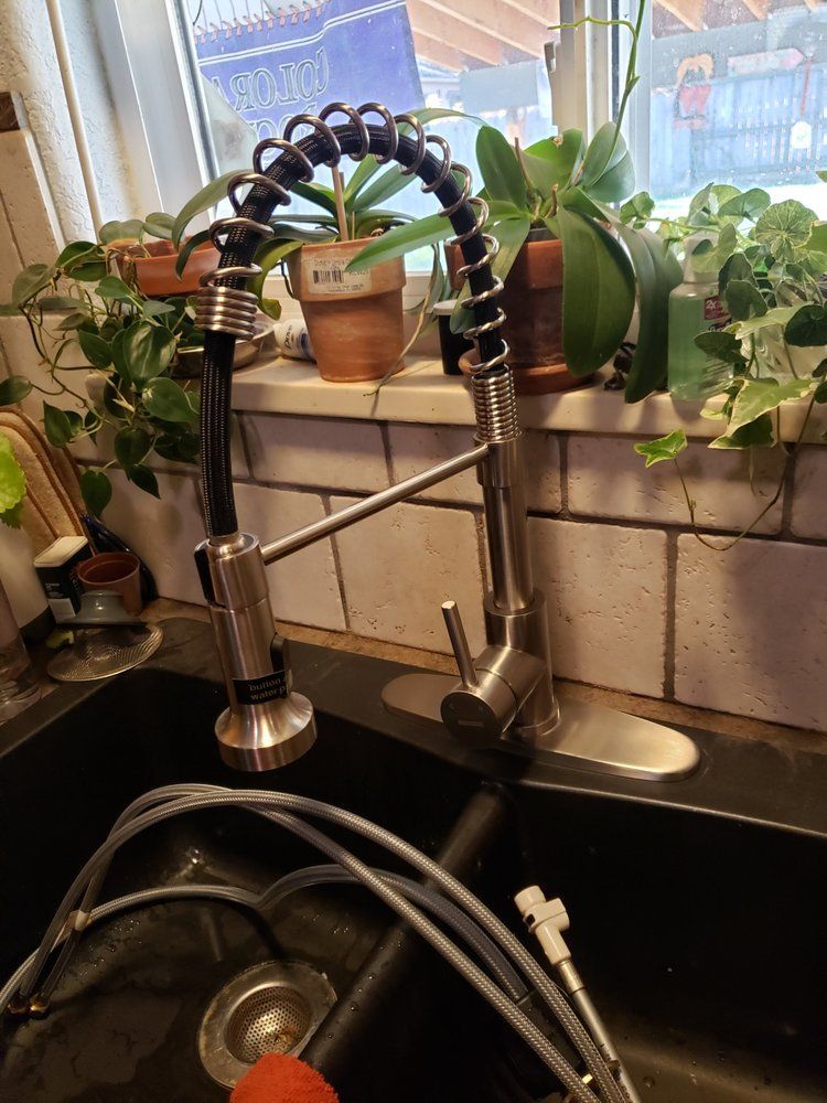 Kitchen sink faucet with coiled spring, houseplants on windowsill, and a dish rack in the foreground