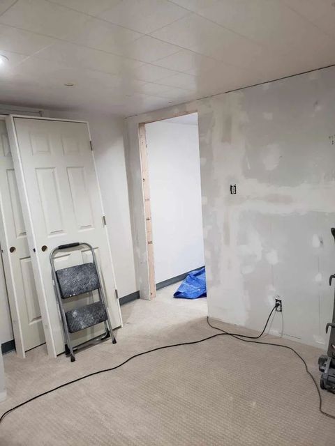 Partially renovated room with drywall, ladder, open doorway, and exposed wires on the floor