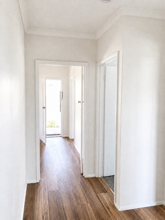 Bright white hallway with wood floors and open doorways leading to a sunlit room — Recoat Painting In West Wodonga, VIC