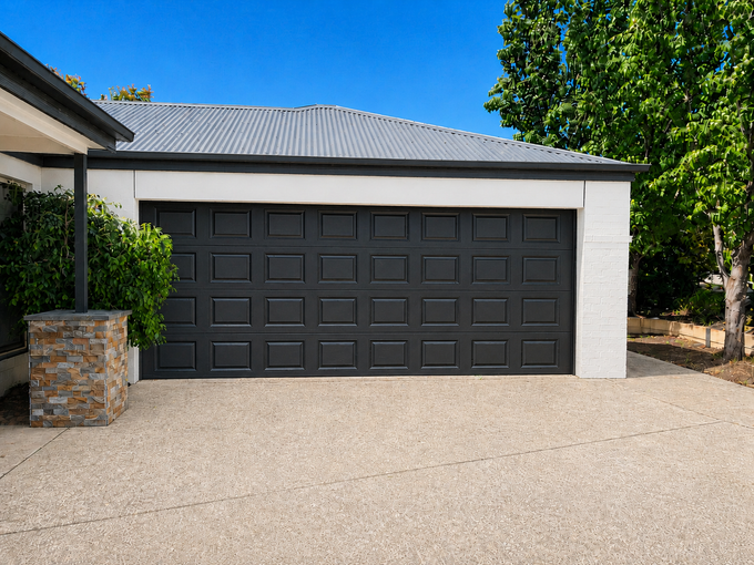 Modern dark garage door on a white house with a gravel driveway and blue sky — Recoat Painting In West Wodonga, VIC