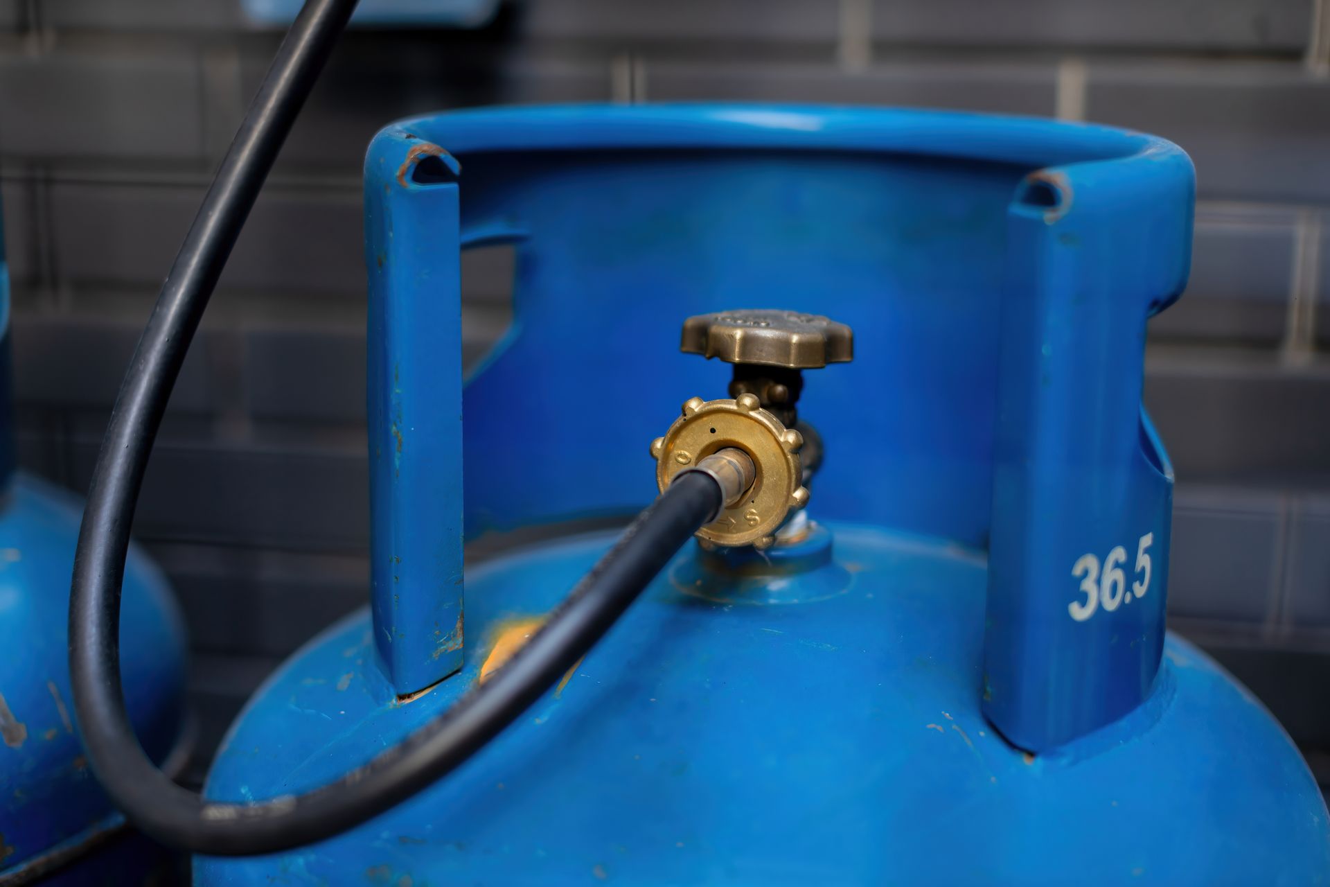 Blue propane tank with black hose attached, against a gray brick wall.