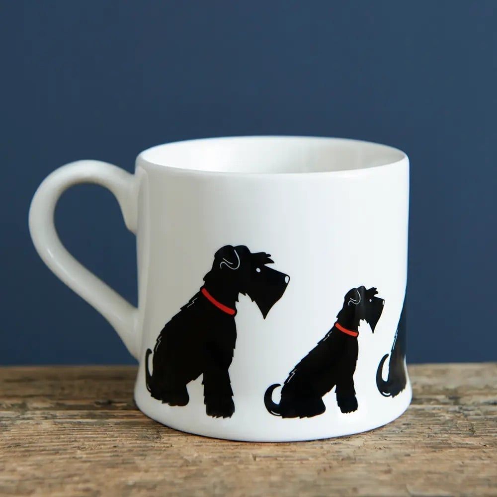 Witte mok met illustratie van een zwarte hond op een kartonnen doos, op een houten oppervlak.