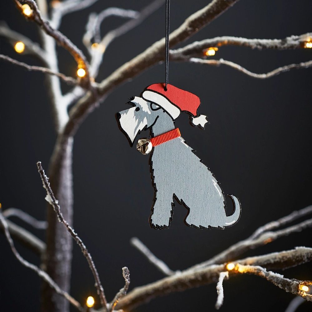 Kerstversiering in de vorm van een schnauzerhond met rode muts en halsband, hangend aan een bevroren boomtak.