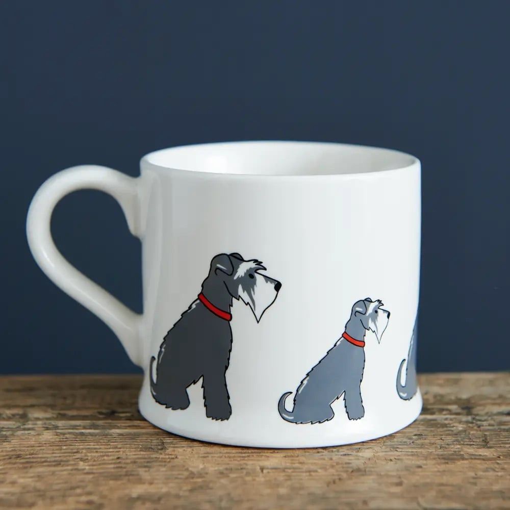 Witte mok met illustraties van grijze honden op een kartonnen doos, op een houten oppervlak.