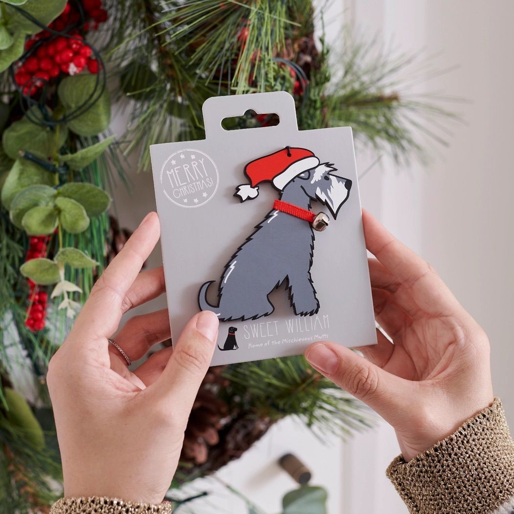 Kerstversiering in de vorm van een schnauzerhond met rode muts en halsband, hangend aan een bevroren boomtak.