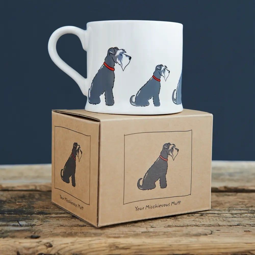 Witte mok met illustraties van grijze honden op een kartonnen doos, op een houten oppervlak.