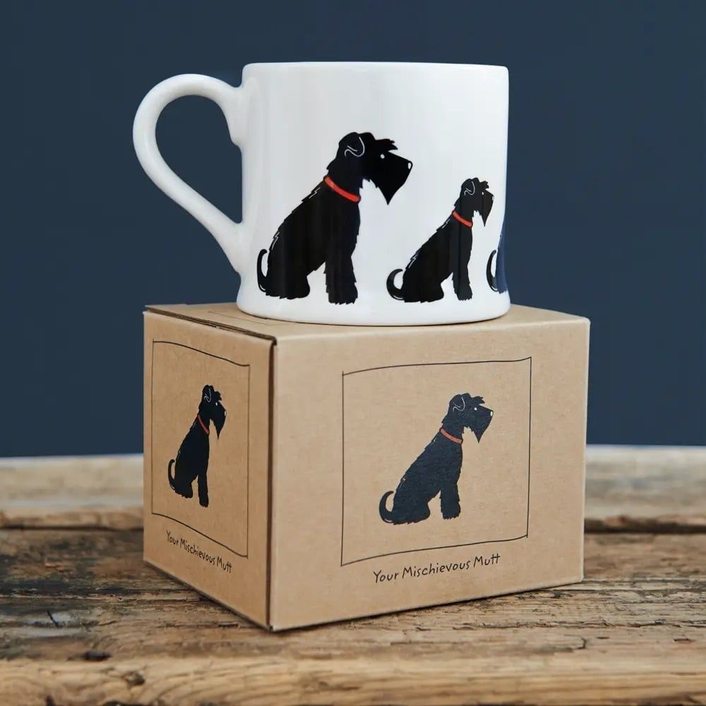 Witte mok met illustratie van een zwarte hond op een kartonnen doos, op een houten oppervlak.