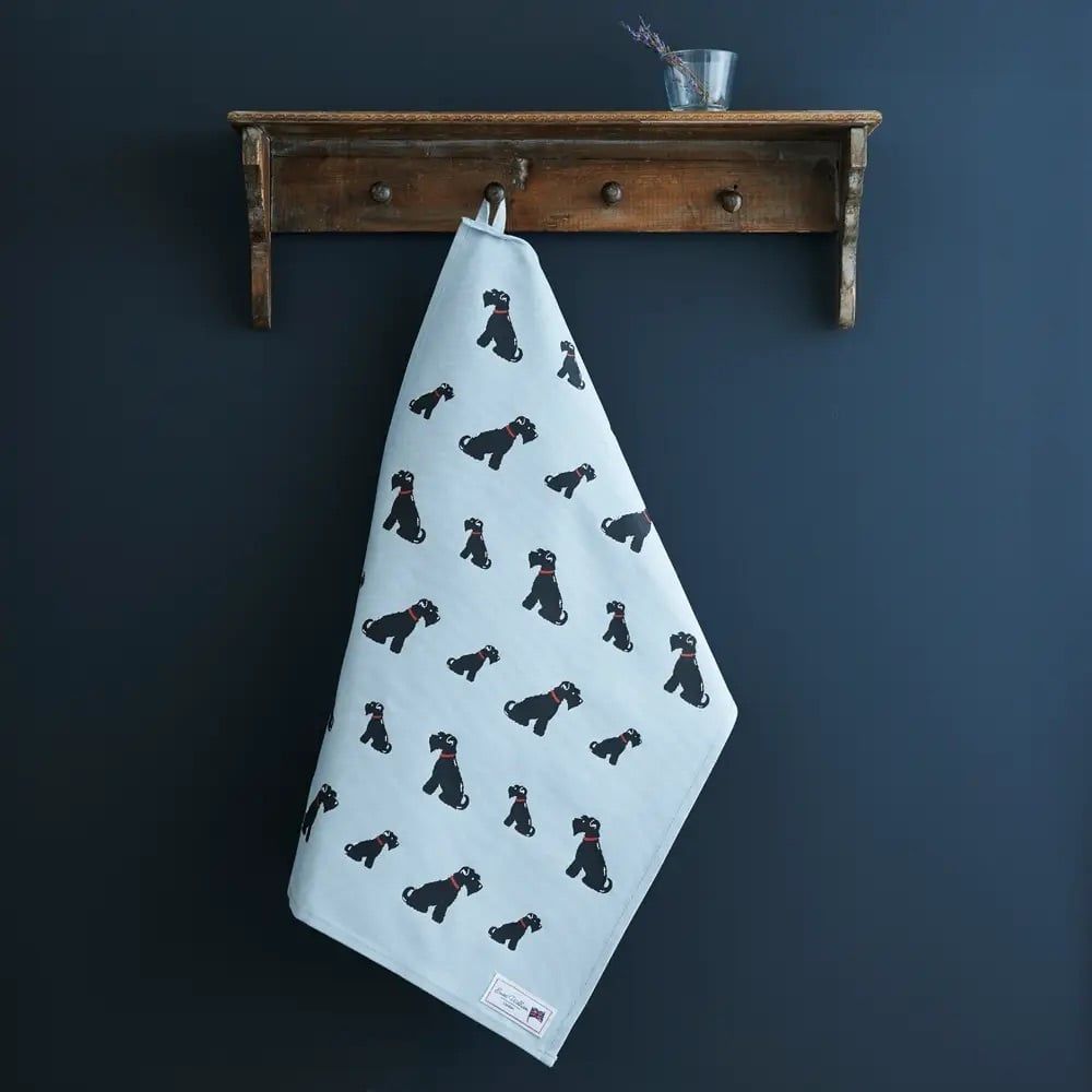 Een blauwe theedoek met hondenmotief hangt op een rustieke houten plank tegen een donkerblauwe muur.