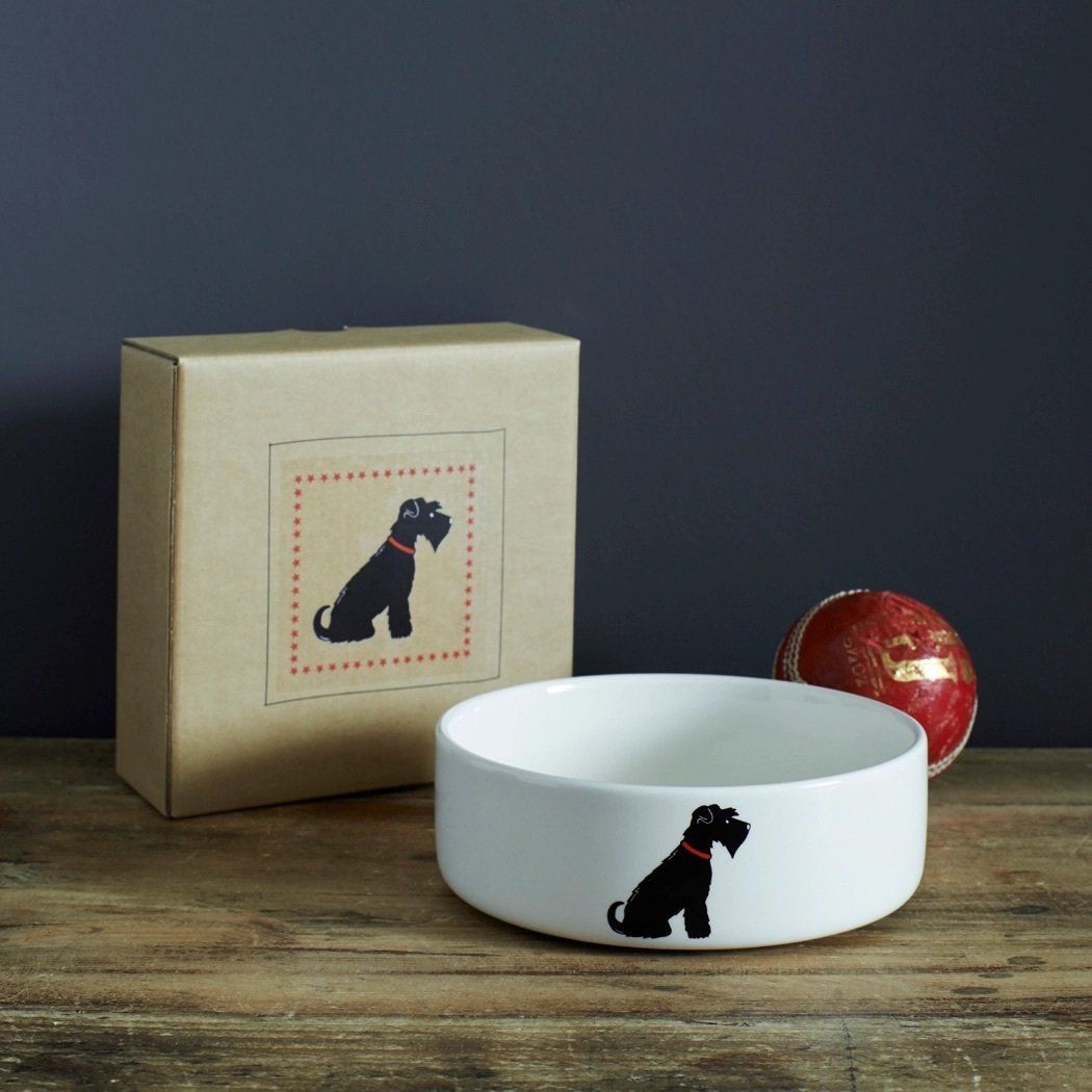 Witte hondenbak met silhouet van een zwarte hond, bruine doos en decoratief ei op een houten oppervlak.