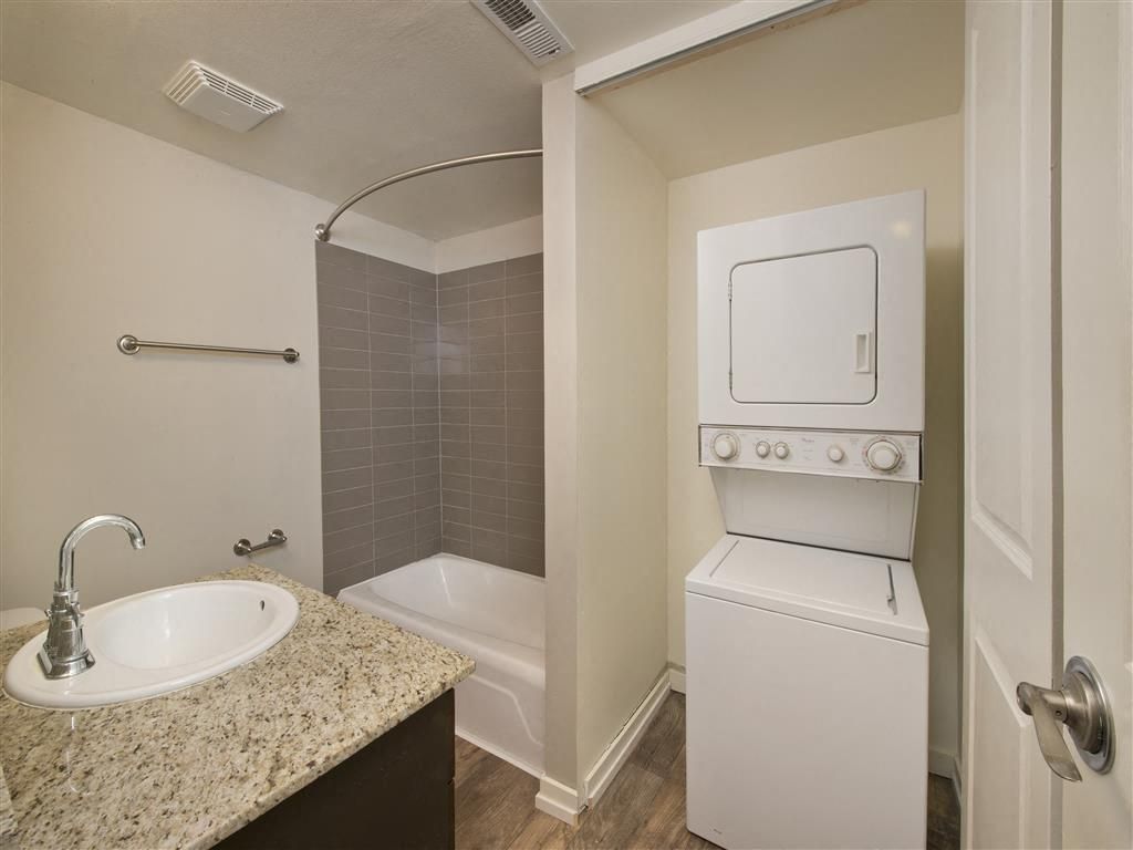 In-unit bathroom with a granite vanity, tub/shower, and a stacked washer and dryer at Harrison Tower