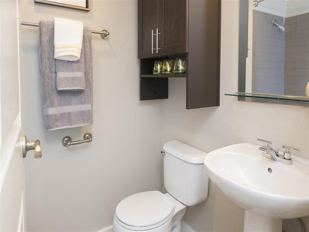 Bathroom with toilet, pedestal sink, mirror, and wall cabinet at Harrison Tower
