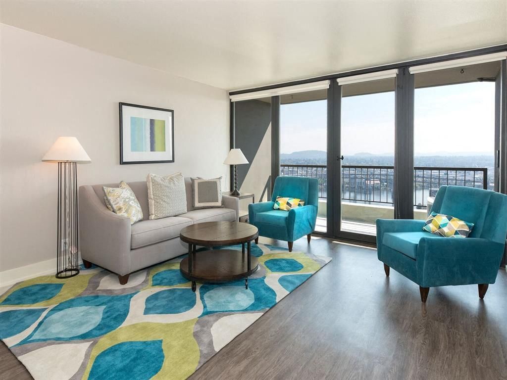 Living room with a grey sofa, two teal chairs, a coffee table, and large doors to a balcony at Harrison Tower