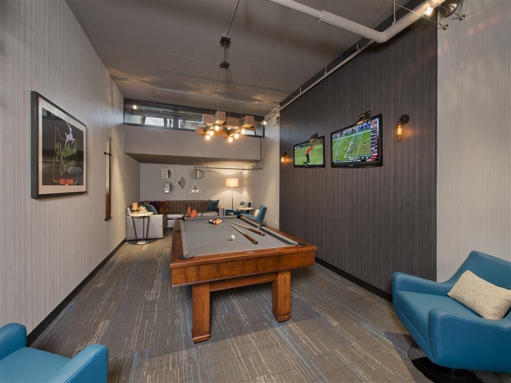 Indoor community game lounge with pool table, seating, and wall-mounted TVs at Harrison Tower