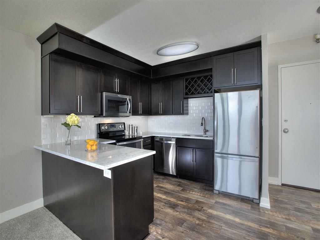 Modern apartment kitchen with dark cabinets, white quartz countertops, and stainless steel appliances at Harrison Tower