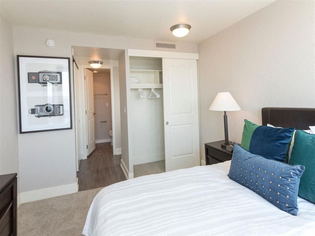 Bedroom in apartment with bed, pillows, nightstand, open closet, and doorway to bathroom at Harrison Tower