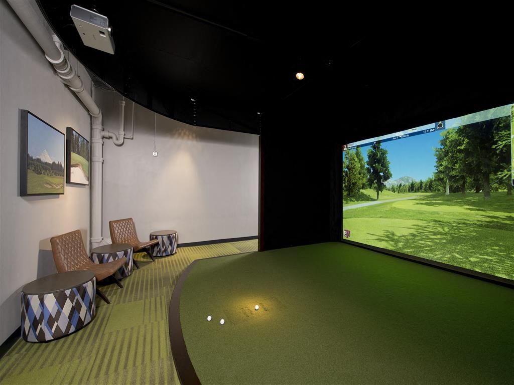 Indoor golf simulator room with a large screen, turf floor, and seating at Harrison Tower