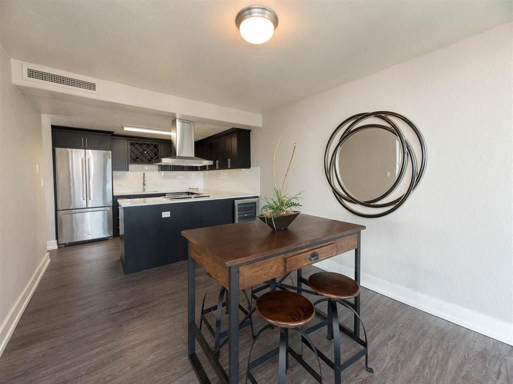 Open-plan kitchen and dining area with stainless fridge, dark cabinets, and a wooden table with stools at Harrison Tower