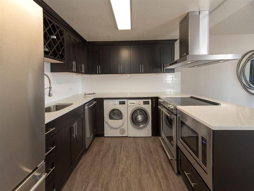 Modern U-shaped kitchen with dark cabinets, white countertops, stainless steel appliances, and a stacked washer/dryer at Harrison Tower