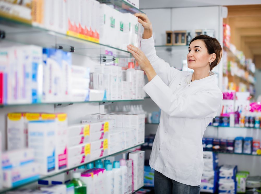A Female Pharmacist is Reaching for a Bottle on a Shelf in a Pharmacy — Bluewater Pharmacy in Yabulu, QLD