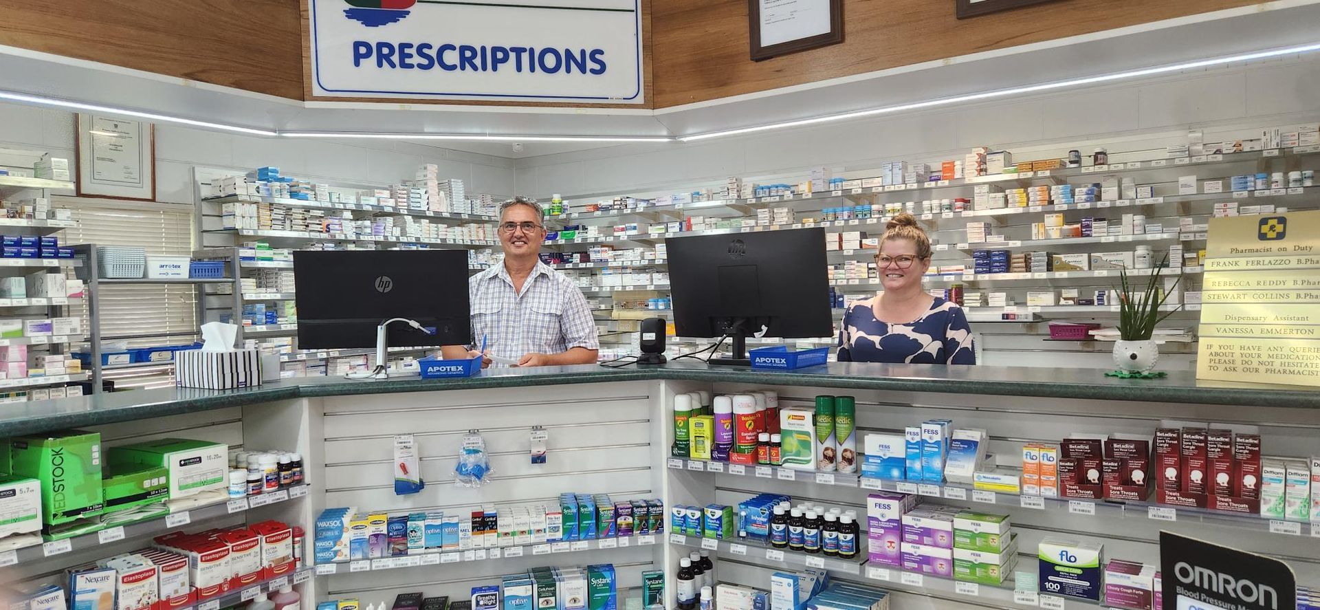 A Pharmacist is Using a Laptop Computer in a Pharmacy While Holding a Bottle of Pills — Bluewater Pharmacy in Jensen, QLD